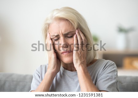 Upset middle aged older woman massaging temples touching aching head feeling strong headache or migraine concept, sad tired stressed elderly senior mature woman suffering from pain or dizziness