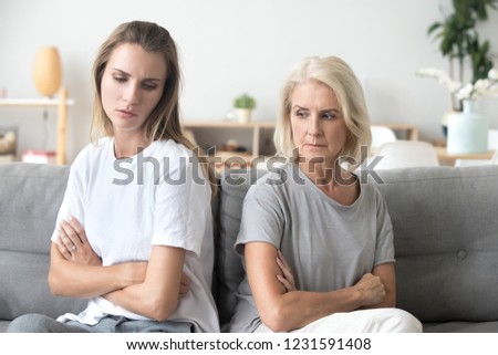 Upset older mother in law and adult daughter sit back to back not talking after fight disagreement, two stubborn old young women ignoring avoiding each other sad by argument, family conflict concept