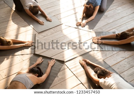 Top above view yoga position Child Pose performed by six diverse young slim yogi females get settled in circle wearing sportswear indoor in the morning. Group training healthy active lifestyle concept