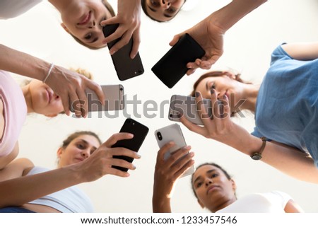 Diverse young women standing together in circle holding smartphones looking at device screen browsing internet, reading email, communicating online, close up focus of arms and gadgets view from below