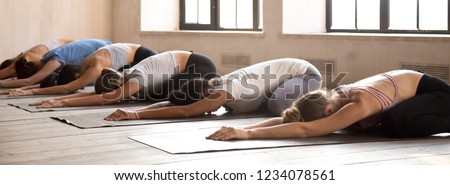Diverse girls energize start new day with yoga session. Sportive females lying resting on rubber mats doing Child Pose, side view. Horizontal photography banner for website header. Wellness concept