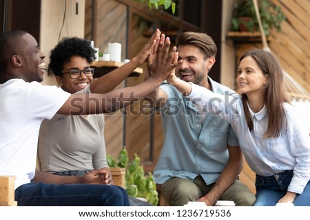 Happy laughing multiethnic friends giving high five, celebrate success together at meeting in cafe, showing support and unity, friendly smiling people joining hands, having fun in coffee house