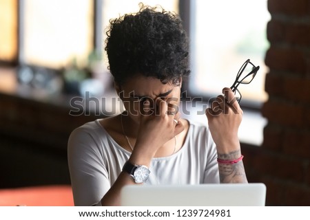 African American woman taking off glasses, feel eye strain, massaging nose bridge, tired female feeling discomfort after long wearing glasses at workplace, work with computer, bad eye vision close up