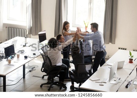 Excited multiracial office workers team giving high five together, celebrating successful teamwork results, involved in team building activity, good corporate relations, motivated by success