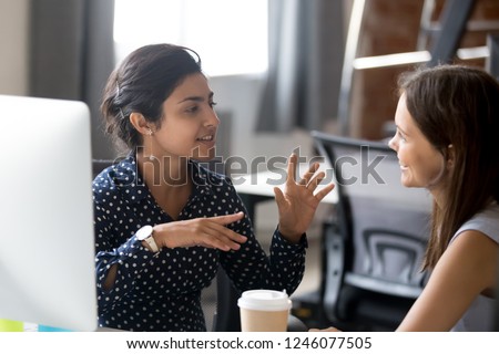 Friendly female colleagues having good relationships, pleasant conversation at workplace during coffee break, smiling young woman listen talkative coworker, discussing new project, talking in office