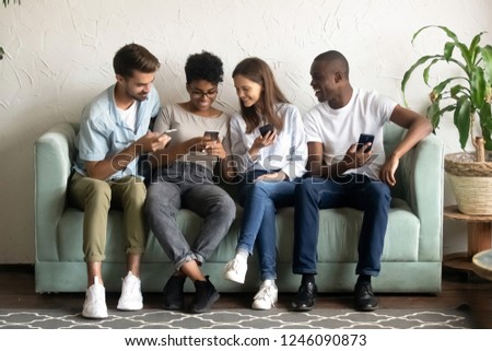 Smiling African American woman show joke on phone to diverse friends, multiracial people using mobile devices together, watching funny video in social network, reading news, look at screen