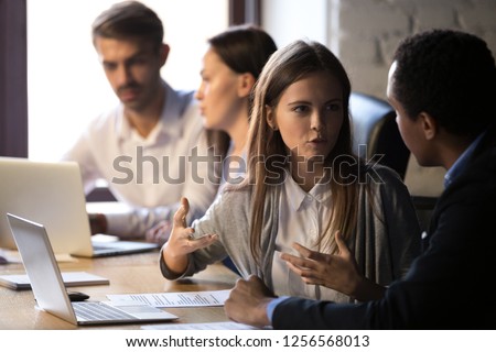 Young caucasian female worker speaking to male african colleague explaining new idea during corporate discussion, diverse coworkers talking working together having business conversation at workplace