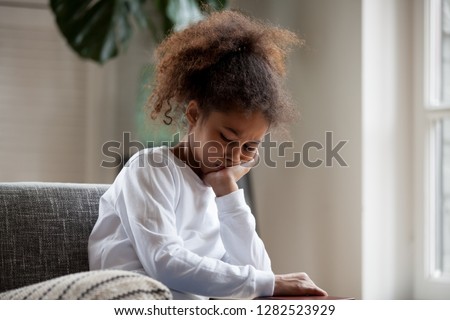 Upset little african american girl feels hurt sad bored sitting alone at home, depressed punished mixed race kid having psychological trauma, frustrated preschool black child thinking hiding problem