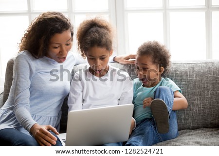 Excited african american mom and mixed race kids looking at laptop surprised with unbelievable online news, amazed black family mother children astonished by huge shopping sale or special email offer