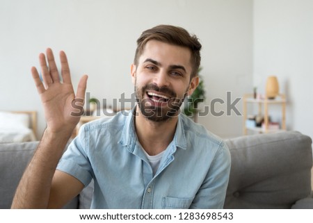 Friendly happy young man waving hand saying hello looking at camera greeting distant friend making online call, cheerful male vlogger blogger recording vlog teaching e-coaching via webcam, portrait
