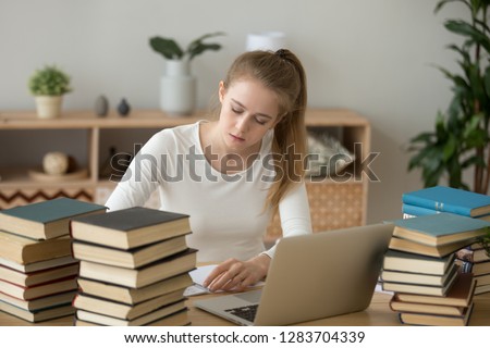 Teen girl preparing for test exam with laptop and books writing essay coursework in notebook studying at home, teenager college student doing research homework assignment making notes learning
