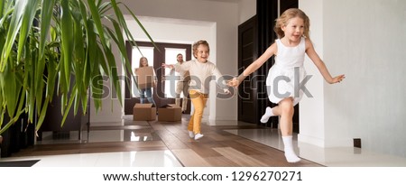 Horizontal photo happy little kids running into new home, parents with cardboard boxes on background. Loan mortgage, moving relocating concept banner for website header design with copy space for text