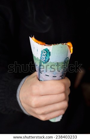 Person grips pack of burning Russian banknotes with nominal value of one thousand rubbles