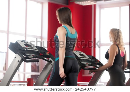 Sporty girls exercising on cardio trainer, treadmill in gym (view from the back)