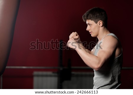 Young caucasian sportsman hit a punch bag, boxing, warming up in fitness center