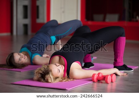 Two pretty girls do aerobics exercises for hips and buttocks in lying position on mats in fitness center
