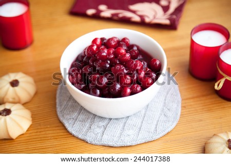 Red berry jam with cookies and red candles on knitted cloth on wooden table, shallow depth of field, focus on top berries