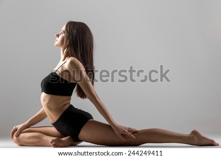 Beautiful sporty yogi girl practices yoga asana, stretching exercises on grey background, low key shot