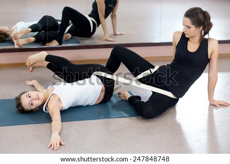 Yogatheraphy. Yoga therapist helps out to Beautiful young woman, two yogi females practicing yoga treatment, doing exercises in class, instructor assists to yogi student