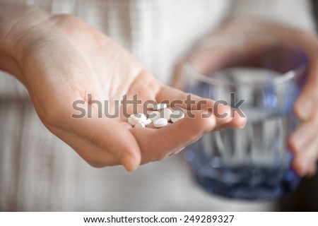 Healthcare, treatment, supplements. Handful of white round pills in female patients palm, woman arm holding heap of small round meds and glass of water, shallow depth of field, focus on medicine