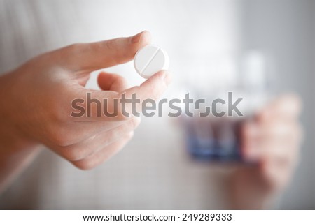 Healthcare, treatment, supplements. Female patient arms holding one round pill and glass of water before taking medication, shallow depth of field, focus on medicine