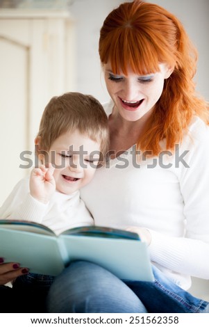 Education. Red-haired young mother reading book to her little son, having fun, laughing together. Focus on child