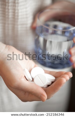 woman arm holding heap of big round meds and glass of water, shallow depth of field, focus on medicine