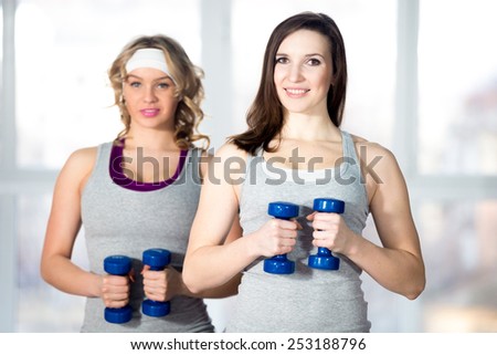 Active, healthy lifestyle, hobby, recreation, wellbeing, weight loss concepts. Two athletic girls doing exercises for waistline, side body bends with dumbbells in class