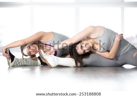 Active, healthy lifestyle, hobby, recreation, wellbeing, weight loss concepts. Two smiling dancer girls stretching, bending bodies to feet during class in white fitness center
