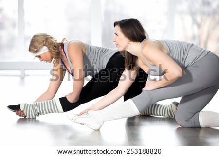 Active, healthy lifestyle, hobby, recreation, wellbeing, weight loss concepts. Group of two athletic girls doing stretching exercises in aerobics class in white room in fitness center