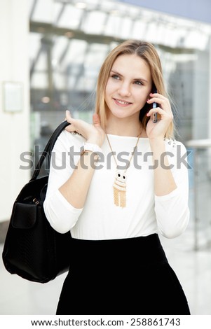 Beautiful smiling young woman wearing fashionable clothes in shopping center, office or college. Using smartphone, making a call