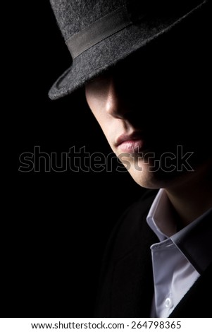 Mysterious man in hat with half of his face in the shadows, minimalistic studio shot against black background, low key lighting