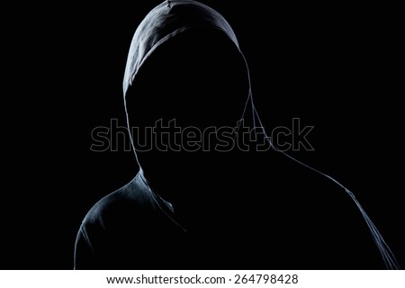Young man in black hooded sweatshirt invisible in the night darkness, dimly lit, concepts of danger, crime, terror