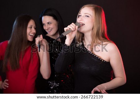 Portrait of beautiful emotional female singer with microphone singing with passion, back vocalists on the background