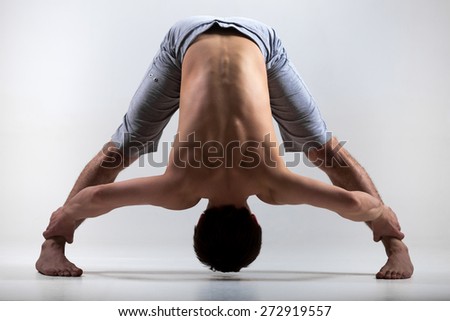 Sporty young man working out, yoga, pilates, fitness training, standing in asana Wide-Legged Forward Bend, Prasarita Padottanasana posture