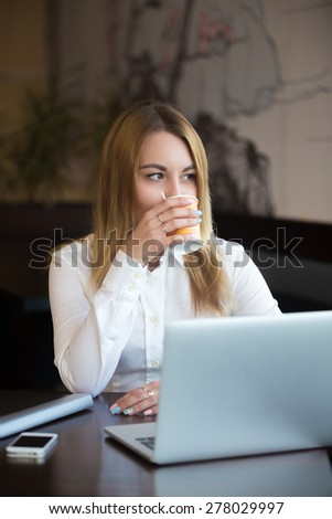 Young beautiful caucasian office woman in formal trendy wear sitting in modern urban cafe tasting her beverage, relaxing after work on laptop