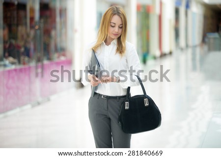 Beautiful business girl wearing office style outfit holding document dossier and suede bag, looking at wristwatch, checking time, running late or waiting
