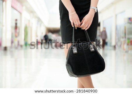 Attractive young woman wearing little black dress holding suede handbag in outlet, close-up