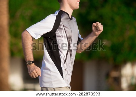 Healthy lifestyle: young sporty man working out outdoors, jogging in summer sunny park, close-up, side view