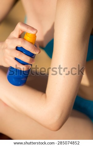 Young woman on the beach holding bottle of suntan lotion, applying sun cream on shoulder before tanning, close up