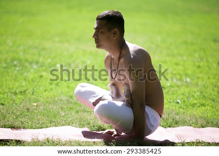 Serene Indian young man in white pants practicing yoga, fitness or pilates on green grass in park, doing arm balance exercise, Scale Pose, Tolasana, utpluthi full length