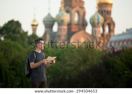 Young handsome traveler man with backpack wearing casual clothes holding map, standing in front Church of the Savior on Spilled Blood in Sent Petersburg, sightseeing, searching for direction