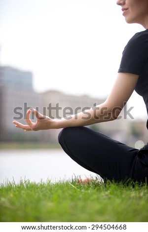 Young smiling office yogi woman sitting cross legged in yoga Easy Sukhasana Pose on river bank in the city, meditating with fingers in Jnana mudra, close up, back view