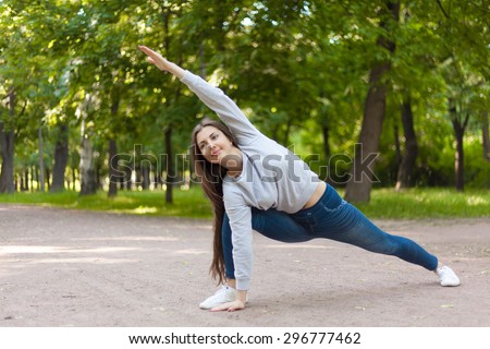 Smiling beautiful sporty young woman working out on road, doing warming up lunge exercise, Utthita Parsvakonasana, Extended Side Angle Pose, full length
