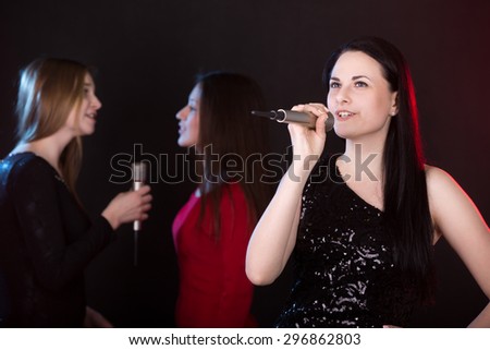 Portrait of beautiful girl singer with microphone singing lyric love song, back vocalists on the background
