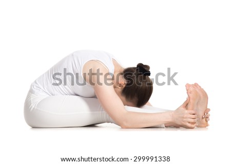 Sporty beautiful young woman in white sportswear sitting in seated forward bend pose, doing paschimothanasana (Caterpillar - yin pose), studio full length shot, isolated