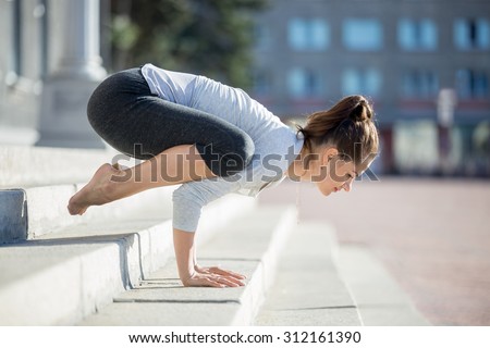 Yoga in the city: beautiful young fit woman wearing sportswear working out on the street on summer day, doing Crane (Crow) Posture, Bakasana (Kakasana), full length, profile view