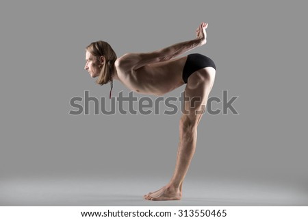 Sporty muscular young yogi man doing easy variation of Standing Half Forward Bend, Ardha Uttanasana pose, studio shot on dark background, side view, full length