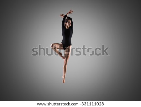 Beautiful young happy smiling fit gymnast woman in sportswear doing art gymnastics, sport practice, dancing, jumping, front view, full length, studio image on gray background