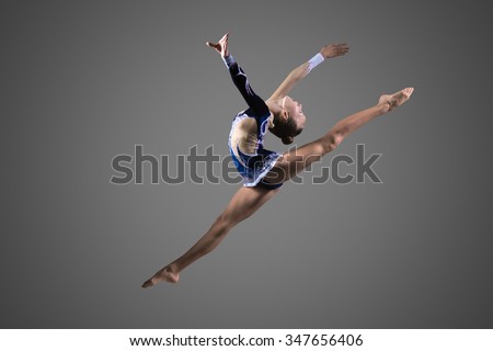 Beautiful cool young fit gymnast woman in blue sportswear dress working out, performing art gymnastics element, jumping, doing split leap in the air, dancing, full length, studio, dark background